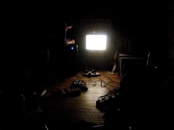 Hastas playing in a dark room, accompanied by visuals on a TV